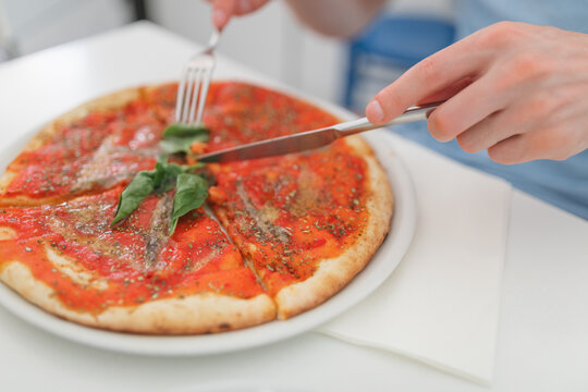 Close-up of a man sitting at a table eating a traditional Italian anchovy pizza