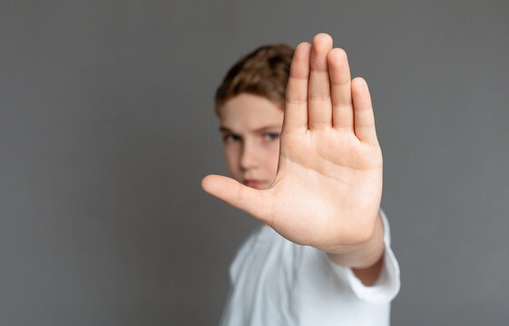 Domestic violence and child abuse. Boy showing stop gesture with his hand, gray background