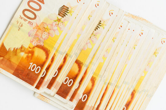 Stack of Israeli shekel banknotes arranged on a white table, representing finance, savings, cash transactions