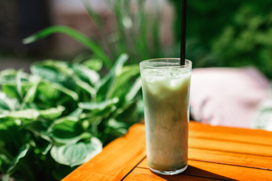 Close-up of an iced matcha latte with a drinking straw on a garden table on a summer day