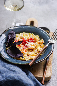 Close-up of a Bowl of ravioletti past, cheese and a glass of white wine on a wooden chopping board