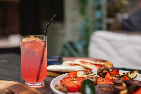 Close-up of a grapefruit lemonade drink and a plate of assorted grilled vegetables at an outdoor cafe