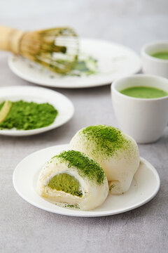Close-up of two Matcha Mochi, two Matcha Lattes and matcha whisk on a table