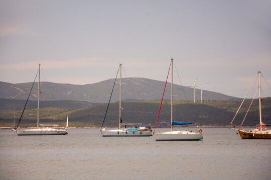 View into land of four Boats moored in the Aegean sea and two Wind Turbines on a hill, Turkey