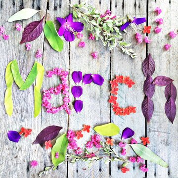 Overhead view of assorted flowers and leaves around the word March spelled out using colourful leaves and flower petals on a wooden table