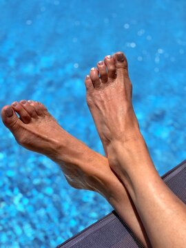 Close-up of a woman's feet with her legs crossed at the ankle on a sun lounger by the swimming pool