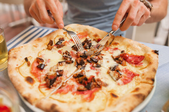 Close-up of a man sitting at a table eating a Neapolitan wood-fired prosciutto ham and aubergine pizza