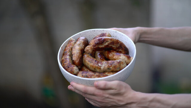 Golden brown grilled sausages with char marks in speckled bowl held by hands. Appetizing bbq food perfect for summer picnics and outdoor cooking 