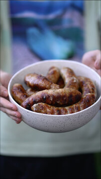 Close-up of hands holding bowl of delicious grilled sausages with crispy skin and juicy inside. Ideal for BBQ, grilling and summer cooking 