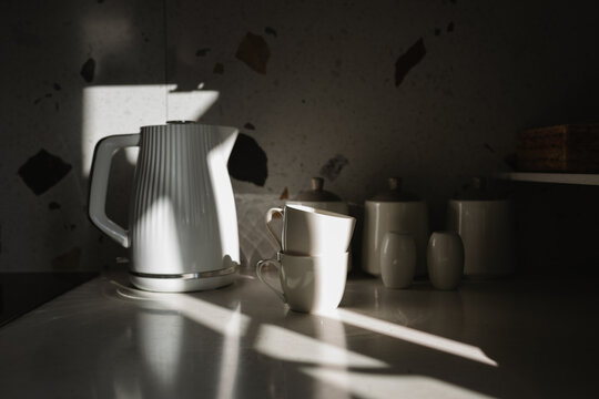 Close-up of a kettle, two cups and jars on a kitchen worktop in the sunlight