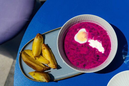Overhead view of a bowl of traditional cold beet soup (chlodnik) served with egg, sour cream and baked potato wedges