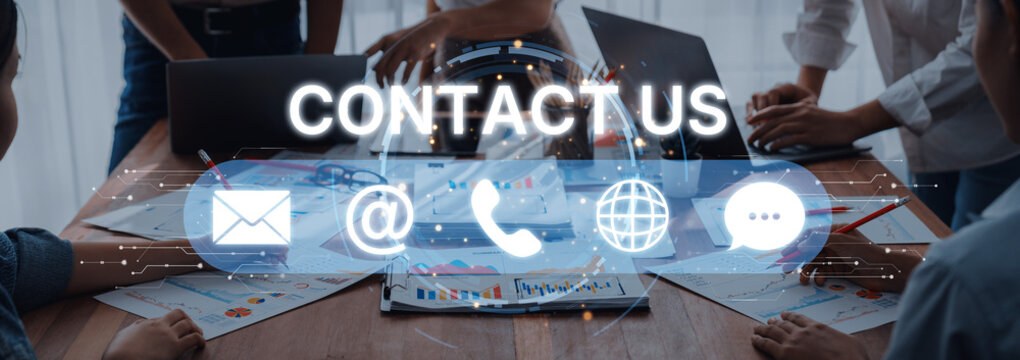 A diverse team working together at a table surrounded by laptops and papers, featuring modern contact symbols representing communication methods in business. Trope