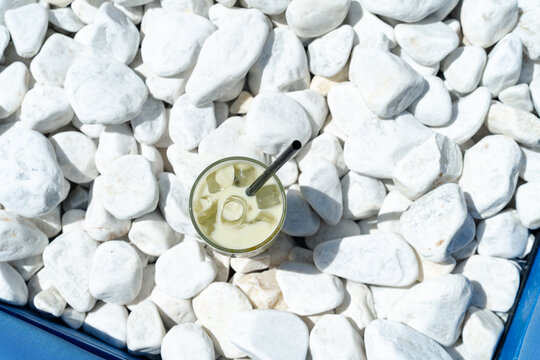 Overhead view of a cold iced mango matcha latte with ice cubes on white stones