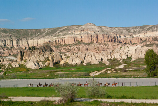 Side view of a row of Horse riders riding past ancient fairy chimney rock formations, Cappadocia, Anatolia, Turkey