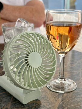 Close-up of a portable electric fan on a table with a glass of rose, a glass of ice cubes and a man sitting in the background