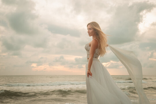 Side view of a young woman in a bustier top and long skirt standing on a sandy beach