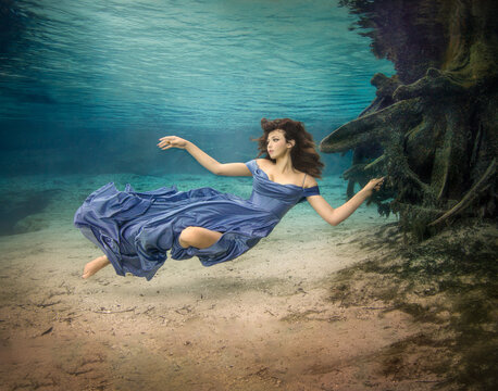 Young woman in a strapless evening gown floating underwater over the seabed