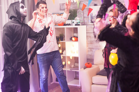Spooky zombie smiles while dancing with a group of people at a Halloween party, mixing horror costume and festive fun, with social party energy, costume interaction.