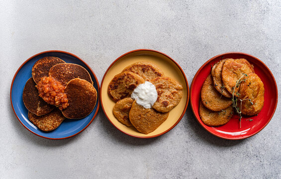 Overhead view of three different coloured plates with Potato pancakes (draniki) and various sauces