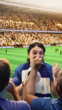 Vertical screen video: Energetic woman shouts through megaphone in stadium, leading football fans during match, with female supporter galvanizing soccer crowd doing loud chants in sports arena.