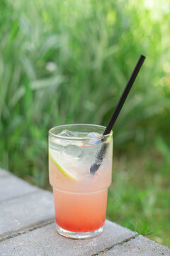 Close-up of a refreshing grapefruit lemonade with ice cubes on a garden ledge