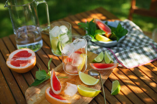 Close-up of a pitcher of water, two Glasses filled with ice cubes, mint leaves and assorted citrus fruit on a garden table in summer