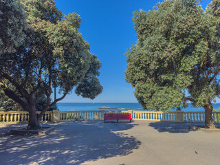 Obraz premium A solitary red bench sits by a stone balustrade framing a stunning ocean view at Praia da Luz in Foz Porto Portugal on a sunny summer afternoon