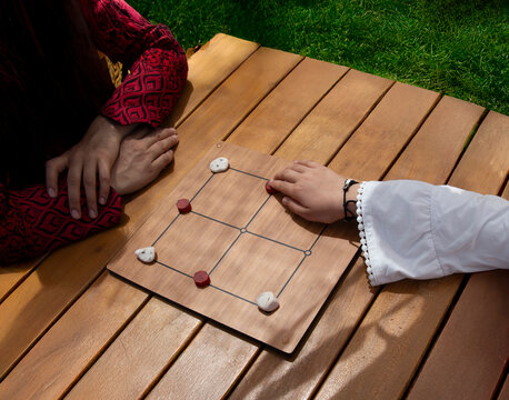 Two people sitting at a table playing the traditional Turkish strategy board game Uc Tas (Three Stones)