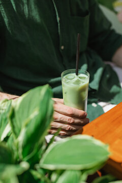 Close-up of a man sitting at a garden table on a summer day drinking an iced matcha latte drink
