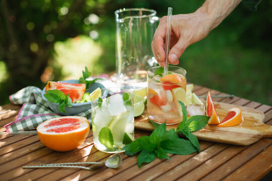 Close-up of a putting a reusable glass straw in a glass of water with mint leaves and assorted citrus fruit