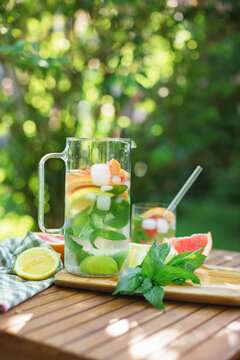 Close-up of a pitcher of water, mint leaves and assorted citrus fruit on a garden table in summer