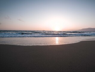Fototapeta premium Peaceful beach at sunset featuring gentle ocean waves, golden light, and a colorful evening sky.