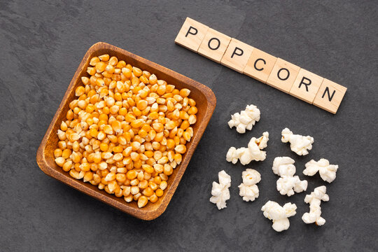Popcorn kernels in a wooden bowl on a background of freshly popped popcorn, ideal for snack and food concepts.