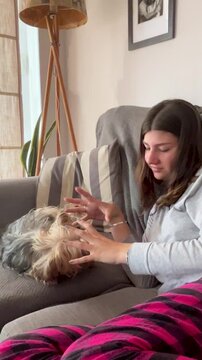 Young woman enjoying quality time with her dog on the sofa, cheerful and relaxed interaction in a bright and modern interior.Vertical 4k video.Cozy and warm home atmosphere.