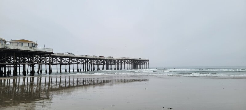 Majestic wooden ocean Crystal pier reflecting on the wet sandy shoreline under a cloudy gray sky in San Diego, California