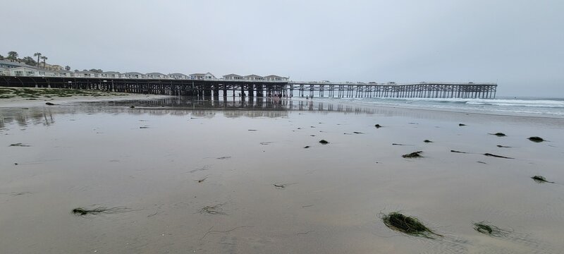Wide low angle view of Crystal Pier and its beachfront cottages reflecting across the wet sandy shore at Pacific Beach, San Diego, California