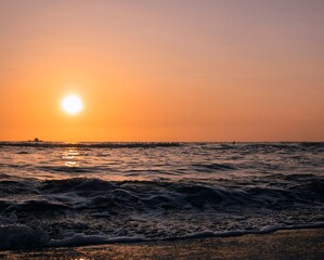 Obraz premium Peaceful beach at sunset featuring gentle ocean waves, golden light, and a colorful evening sky.