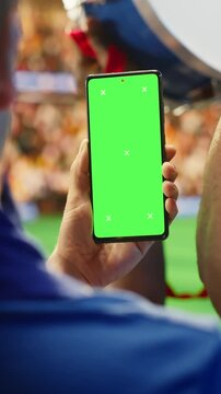 Vertical video: Close-up of mockup phone used by fan in stadium to compare odds during soccer match day for sports betting, editable screen and fan reaction content.