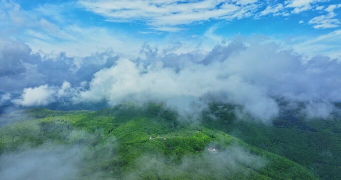 Aerial View of Misty Green Mountains and Forested Hills Beneath a Dramatic Cloud Sky