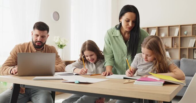 Family parents mother father daughters studying homework together. At a home desk parents guide children with learning as girls write, father on laptop. Theme is family education and support.