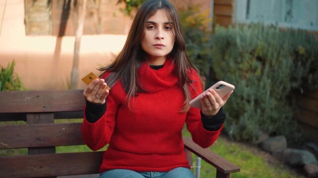 Young Hispanic woman outdoors feeling frustrated about her finances after being unable to complete an online purchase with her credit card, showing financial stress and digital payment issues.
