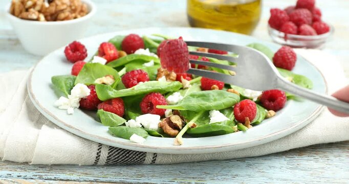woman eating appetizing salad with spinach, cheese, walnuts and raspberries at table, closeup