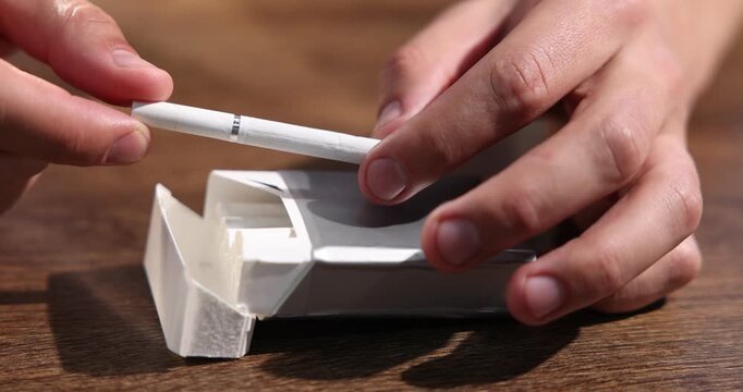 Man with pack of cigarettes at wooden table, closeup