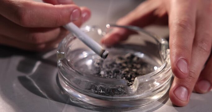 Man flicking ash from cigarette into ashtray at grey table, closeup