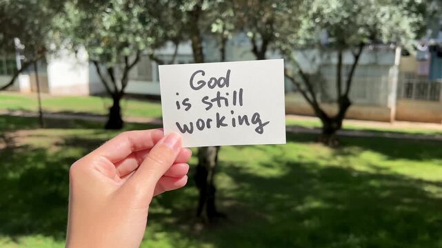 Hand with christian faith motivational concept - God is still working, on the nature background