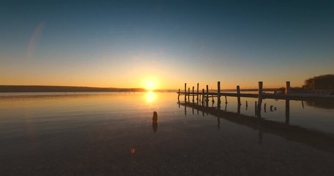 Sea horizon and color sunset over water and wooden fishing pier near the shore

