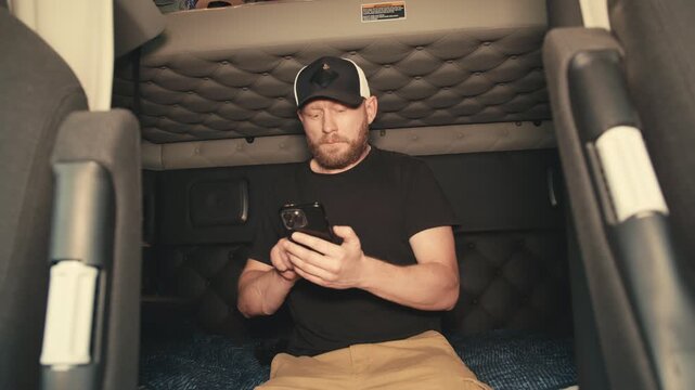 Truck driver resting and using smartphone in sleeper cab