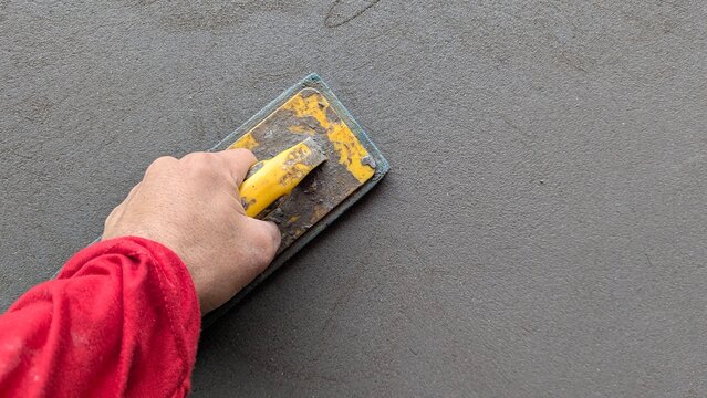 Hand worker applying fresh wet cement mortar with steel trowel on concrete wall background with copy space