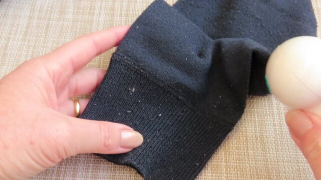 Closeup of female hands carefully using an electric lint remover to clean pills and fuzz from a blue sweater. Housework and garment care concept.