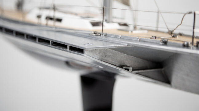 Close up of a scale model sailboat showing metal hull and wooden deck